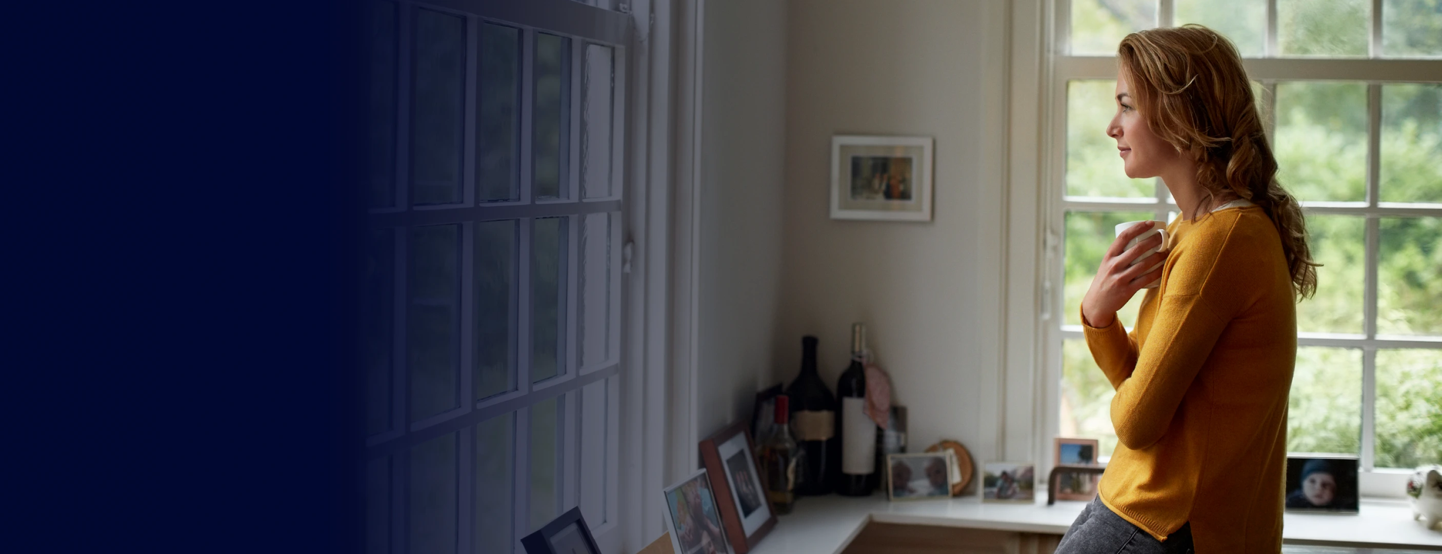 Photo of a women holding a coffee cup looking out the window